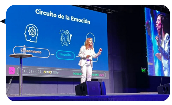 Natalia De Vita en el escenario durante una conferencia, explicando el "Circuito de la Emoción" con una presentación visual de fondo.