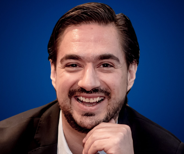 Carlos González sonriendo en un fondo azul.