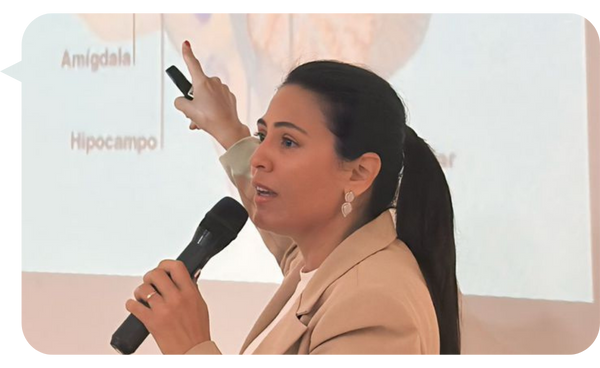 Fabiana Matos explicando conceptos de neurociencia en una conferencia, señalando áreas del cerebro en una proyección.